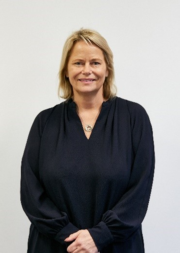 Cheryl Rhodes, a white woman with mid-length blonde hair, wearing a black dress 